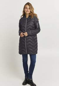Mørkegrå polstret jakke med et chevron-quiltmønster, lynlåslukning og sidelommer, parret med mørke jeans og sorte ankelstøvler.