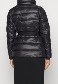 Svart pufferjacka med en kviltad design, med en bälte i midjan, hög krage och mjuk textur. Inkluderar elastiska ärmslut och en figursydd siluett.