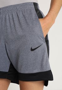Sportovní šortky Nike, vyrobené ze šedé texturované látky, s černým lemováním, bočními kapsami a černým logem na levé noze.