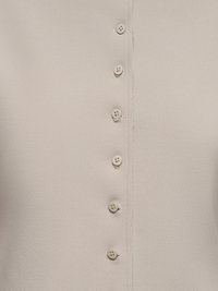 Gros plan sur un tissu texturé beige clair avec une rangée verticale de six petits boutons ronds beige fixés au centre.
