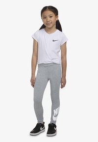Hvit Nike T-skjorte med korte ermer og svart logo, kombinert med grå tights med stor hvit "NIKE"-tekst, og svarte treningssko.