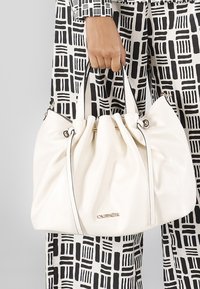 Borsa in pelle bianca con design arricciato, due manici corti, accessori in metallo dorato e una bordatura nera a contrasto.