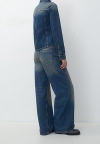 Conjunto de chaqueta de mezclilla y jeans de pierna ancha en azul medio con un acabado decolorado. Presenta botones en la chaqueta y dos bolsillos traseros en los jeans.