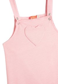 Vaaleanpunainen, teksturoitu haalari, jossa on sydämenmuotoinen aplikaatio, metallinapeilla olkaimissa, valmistettu pehmeästä puuvillasta. Tagi kertoo "valmistettu babin toimesta."