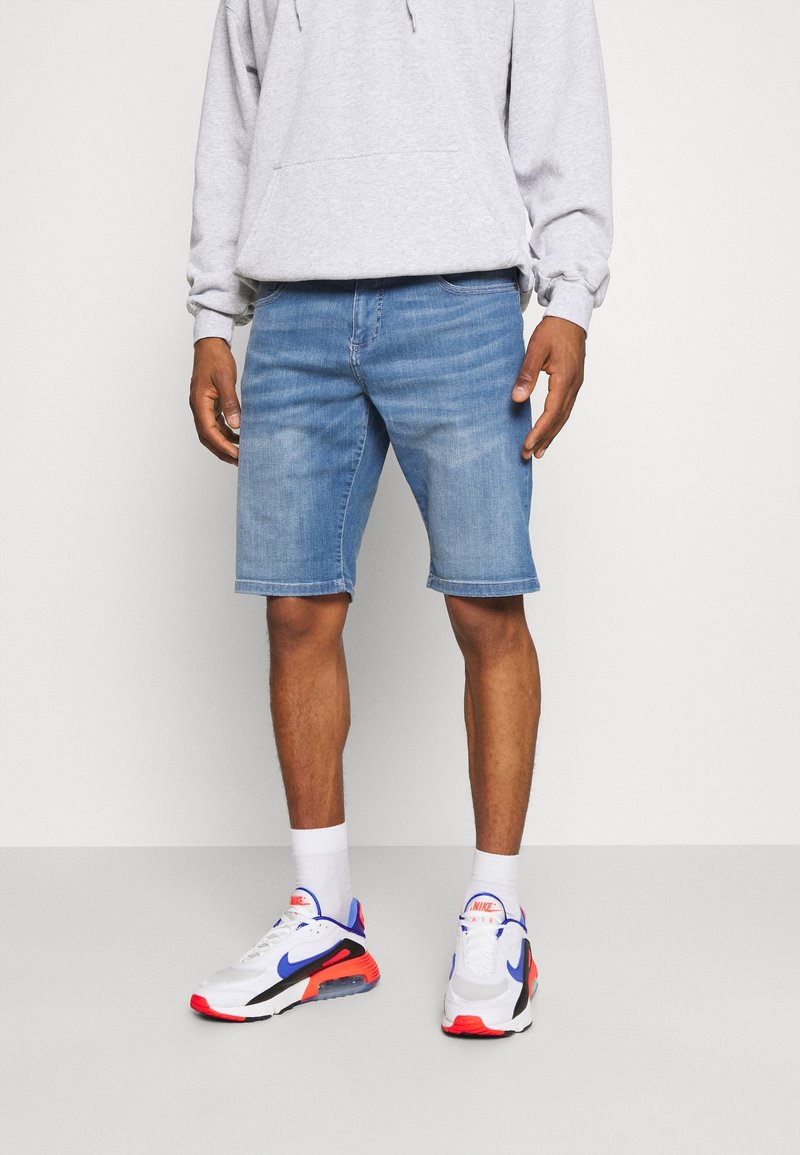 Shorts de mezclilla en azul claro, con un corte recto y un ligero desvanecimiento. Combinados con una sudadera gris y zapatillas blancas con acentos rojos y azules.