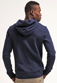 Navy blue hooded sweatshirt made of soft cotton blend, featuring a kangaroo pocket, ribbed cuffs, and hem, with a smooth textured finish.