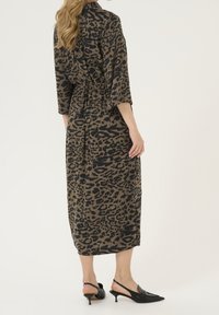 Robe midi à imprimé léopard dans des tons de marron et noir, avec des manches 3/4, une taille élastique, et associée à des escarpins noirs à bride arrière.