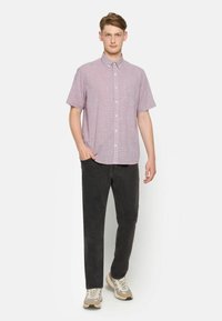 Camisa de cuadros en color púrpura claro, de manga corta, con collar tipo button-down y un bolsillo en el pecho, combinada con jeans negros y zapatillas beige.