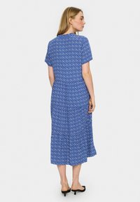Rochie midi cu un model albastru, cu mâneci scurte, având un design geometric, material fluid și un tiv în straturi. Vedere din spate.