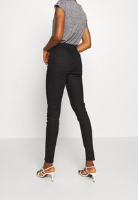 Svarta skinny jeans med hög midja, med en slät textur, fem fickor och en liten logotagg. Bärs med vita sandaletter med remmar.