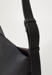 Fekete bőr válltáska, texturált felülettel, állítható pánttal és sima belső térrel. Minimalista design, látható hardver nélkül.