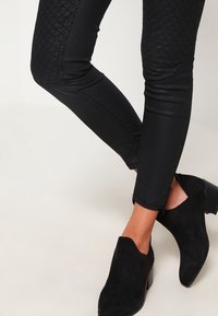 Svarta smala byxor med kviltade paneler och en slät yta, matchade med svarta mocka ankelboots med en kraftig klack.