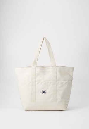 Borsa in tela di colore bianco sporco con due manici robusti, presenta un'etichetta circolare e cuciture orizzontali sul davanti.