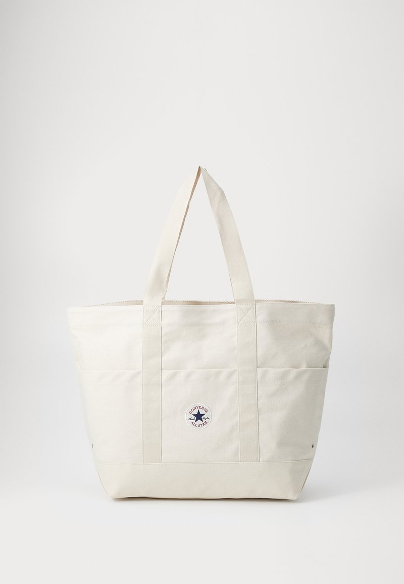 Borsa in tela di colore bianco sporco con due manici robusti, presenta un'etichetta circolare e cuciture orizzontali sul davanti.