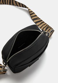 Sort stof crossbody tas med lynlås lukning. Har en mønstret beige og sort rem og en glat overflade. Indvendigt ser det uforet ud.