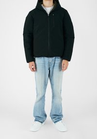 Sorte puffervest med hætte, lynlås foran og sidelomme. Sammen med lyseblå slidte jeans og hvide sneakers.