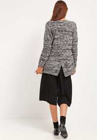 Pull en tricot gris et noir, à manches longues, en tissu texturé, avec une fente sur le côté au dos, associé à des culottes noires et des ballerines.