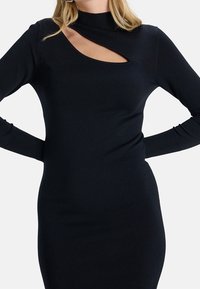 Abito a maglia nero aderente con scollatura alta e un dettaglio a taglio diagonale sulla clavicola, maniche lunghe e texture morbida.
