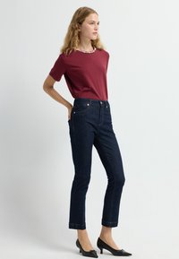 Vínová tričko s krátkým rukávem, vysoké tmavé džíny a černé lodičky s špičatou špičkou. Obsahuje jemné švy a přiléhavý siluetu.