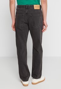 Pantalones de mezclilla negros con un corte relajado, que cuentan con dos bolsillos traseros y una etiqueta de cuero marrón en la cintura. Tejido texturizado.