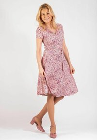 Kukkakuosisessa mekossa on vaaleanpunaista ja valkoista, lyhyet hihat, kietaisumalli ja solmittava vyö vyötäröllä. Parina vaaleanpunaiset kengät.