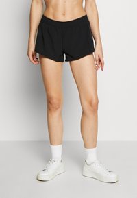 Shorts de sport noirs avec une taille élastique, présentant une coupe ample et une doublure blanche contrastante à l'intérieur de la cuisse. Associés à des baskets blanches.