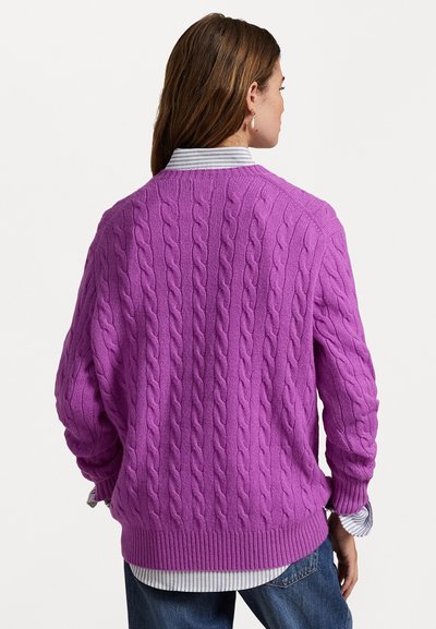 Paarse kabelgebreide trui met een ronde hals en een geribde zoom. Draagt boven een gestreept shirt, het textuurontwerp bedekt het hele kledingstuk.