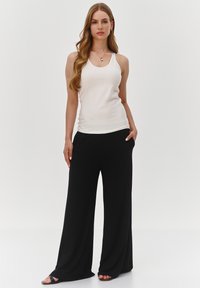 Biały top na ramiączkach z cienkimi paskami w połączeniu z luźnymi czarnymi spodniami o szerokich nogawkach. Tkanina wydaje się gładka i miękka. Całość dopełniają czarne sandały.