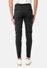 Pantaloni neri slim-fit in cotone con una superficie liscia. Due tasche posteriori con cerniera, abbinati a sneaker bianche.