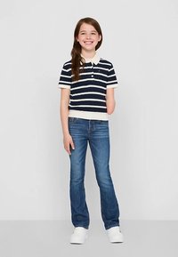 Tumesinise ja valge triibuline lühikeste varrukatega polosärk, millele on kombineeritud sinised teksad ja valged spordijalatsid. Särgil on krae ja nööpidega detail.