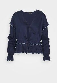 Blusa blu navy con maniche a volant, bordi scallop e chiusura a fiocco. Tessuto leggero con una finitura texture e vita aderente.