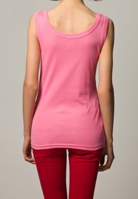Roze katoenen tanktop met een ronde halslijn en brede schouderbanden, gecombineerd met rode broek, die een snug fit en een soepele textuur toont.
