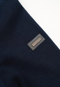 Marineblaue Strickware mit strukturiertem Muster, ausgestattet mit einem grauen Etikett mit geprägtem Text auf einem rechteckigen Patch.