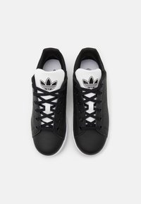 Zapatillas de cuero negro con acentos blancos, con una parte superior texturizada, punta redonda y un diseño con cordones. Logo de Adidas en la lengüeta.