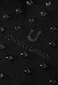 Sort stof med hævede cirkulære teksturer og et mat logo, der læser "JOHNNY URBAN." Accenter reflekterer lys med en blank finish.