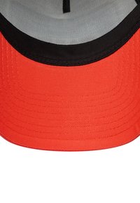 Casquette de baseball rouge avec une visière noire. L'intérieur présente une doublure grise et un tissu texturé, avec des coutures visibles le long de la bordure.