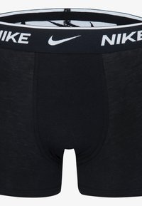 Črne bombažne boksarice z belim logotipom Nike na elastičnem pasu. Imajo prilegajočo se zasnovo in gladko teksturo.