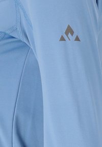 Hellblaues Sportshirt mit glatter Textur, mit genähten Details und einem kleinen grauen Logo auf dem Oberarm.