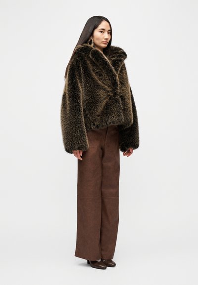 Καφέ κοντό μπουφάν  από ψεύτικη γούνα με φαρδύ γιακά, σε συνδυασμό με καφέ παντελόνι ψηλόμεσο, φαρδύ, και καφέ μυτερά παπούτσια. Λείο ύφασμα.