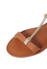 Sandalo in pelle color nocciola con una superficie texturizzata sulla fascia, caratterizzato da un sottile accento in metallo dorato e una suola marrone liscia.