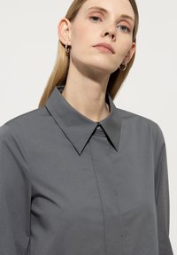 Graues Hemd mit Knopfverschluss und spitzem Kragen, aus glattem Stoff, mit minimalistischem Design und feiner Textur.