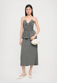 Γκρίζο τοπ με πιέτες σε στυλ peplum, συνδυασμένο με μια ταιριαστή μίντι φούστα που έχει μαύρα διαμαντένια σχέδια. Αξεσουάρ περιλαμβάνουν μια κρέμα τσάντα και λευκά μούλ.