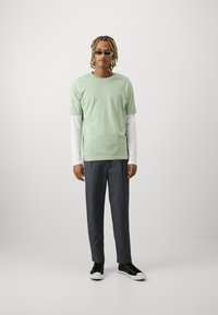 Lichtgroene t-shirt met korte mouwen, over een witte overhemd met lange mouwen, gecombineerd met donkergrijze broek en zwarte sneakers met witte zolen.