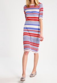 Neulemekko, jossa on vaakasuorat raidat punaisena, sinisenä ja kermaisen värisenä. Lyhyet hihat, pyöreä pääntie, polven mittainen ja teksturoitu kangas.