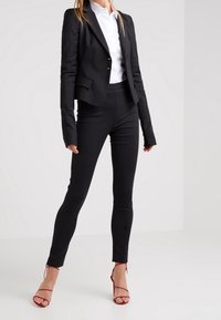 Svart skräddarsydd kavaj över en vit skjorta, ihop med svarta figurnära byxor och röda sandaletter med remmar. Slät tyg med skräddarsydd passform och subtila detaljer.