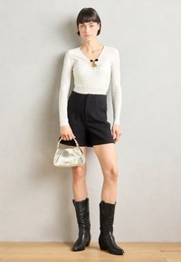 Long-sleeve ivory bodysuit with a V-neck and black accent, paired with high-waisted black shorts and silver handbag, and black cowboy boots.