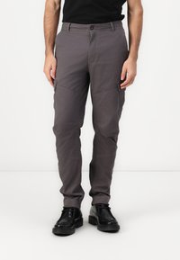 Pantalones cargo grises de tela, con bolsillos laterales, diseño de pierna recta y cierre de botón en la cintura. Llevados con zapatos negros.
