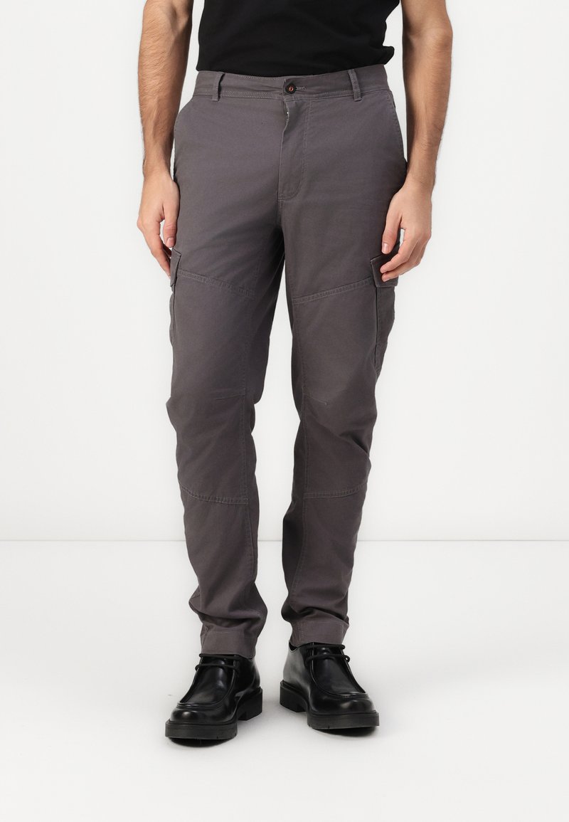 Pantalones cargo grises de tela, con bolsillos laterales, diseño de pierna recta y cierre de botón en la cintura. Llevados con zapatos negros.