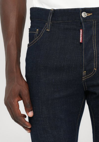 Dark blue denim jeans with yellow stitching, a classic five-pocket design, and a visible brand tag on the waistband.
