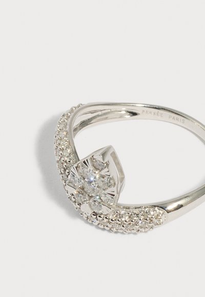 Ασημένιο δαχτυλίδι με σύμπλεγμα λαμπερών διαφανών λίθων σε ανθική διάταξη και υφασμένη μπάντα, με εγχάρακτη την επιγραφή "PERSÉE PARIS" στο εσωτερικό.